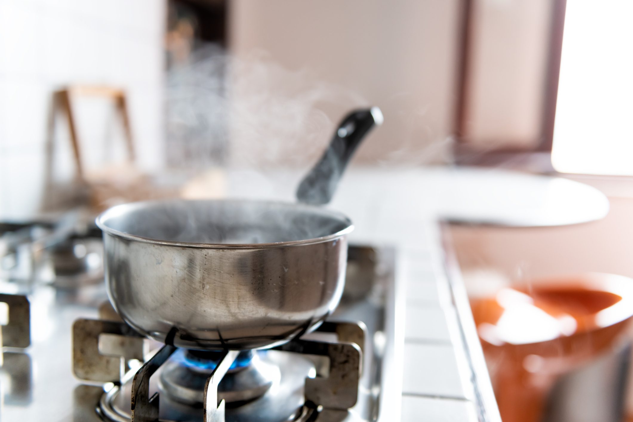 Closeup of vintage tiled gas stove top with tiles white countertop and stainless steel pot and steam cooking with blue flame in retro kitchen