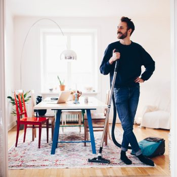 Happy Man Standing With Vacuum Cleaner In Dining Room At Home