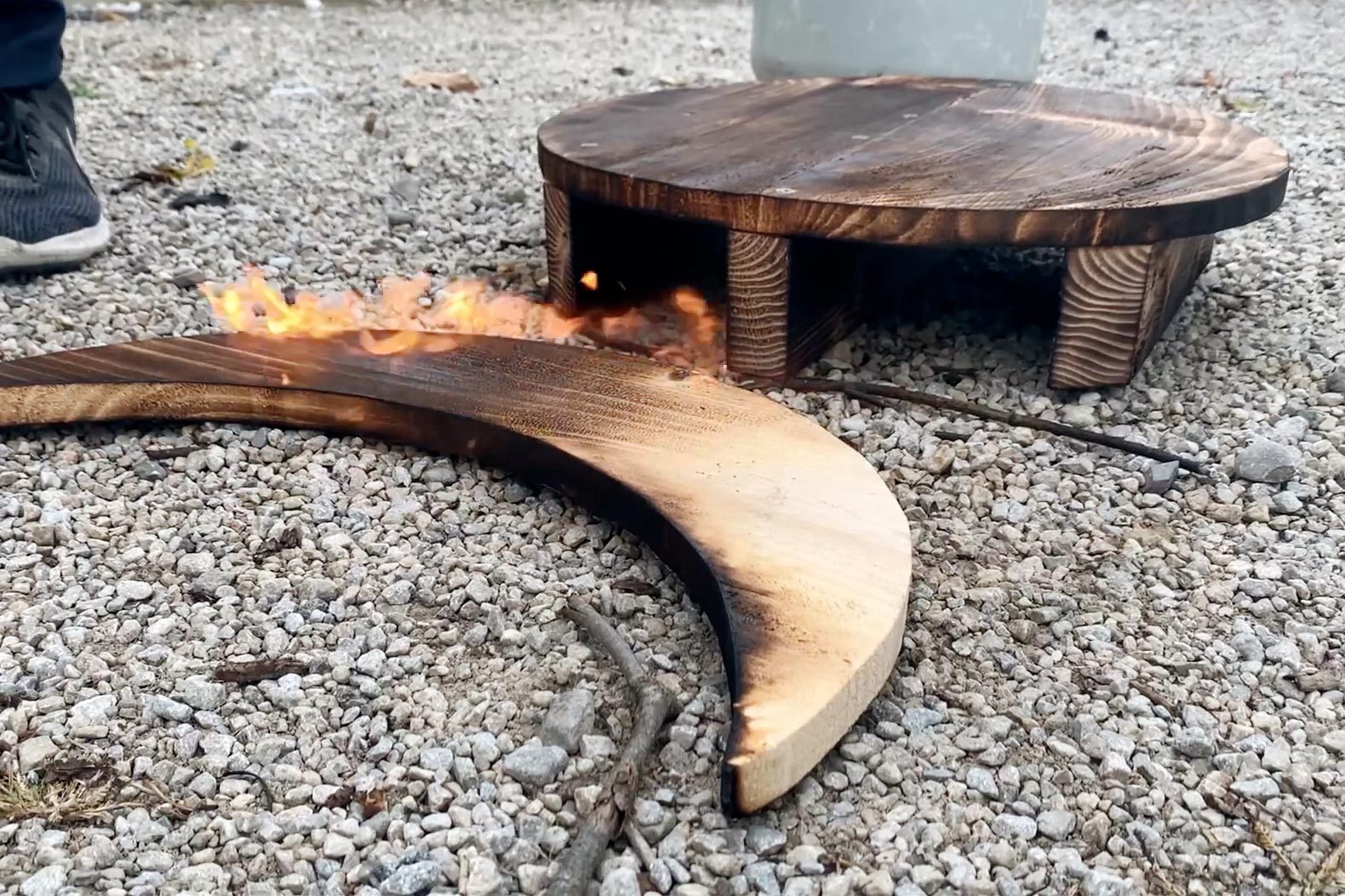 a moon shaped piece of wood burning on a gravel ground