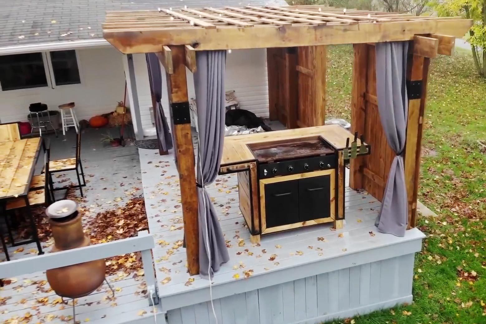 a patio with a grill and wooden pergula