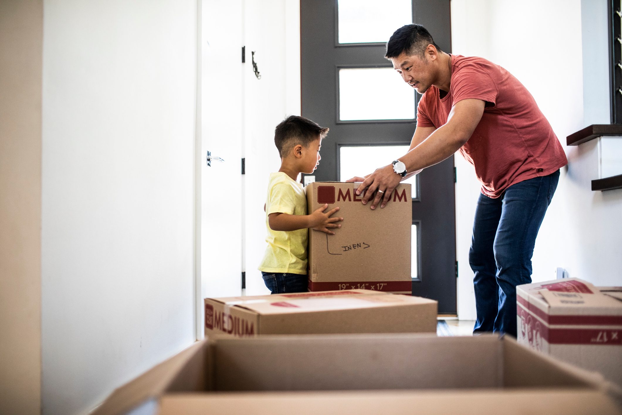 Father and son lifting moving boxes at new home