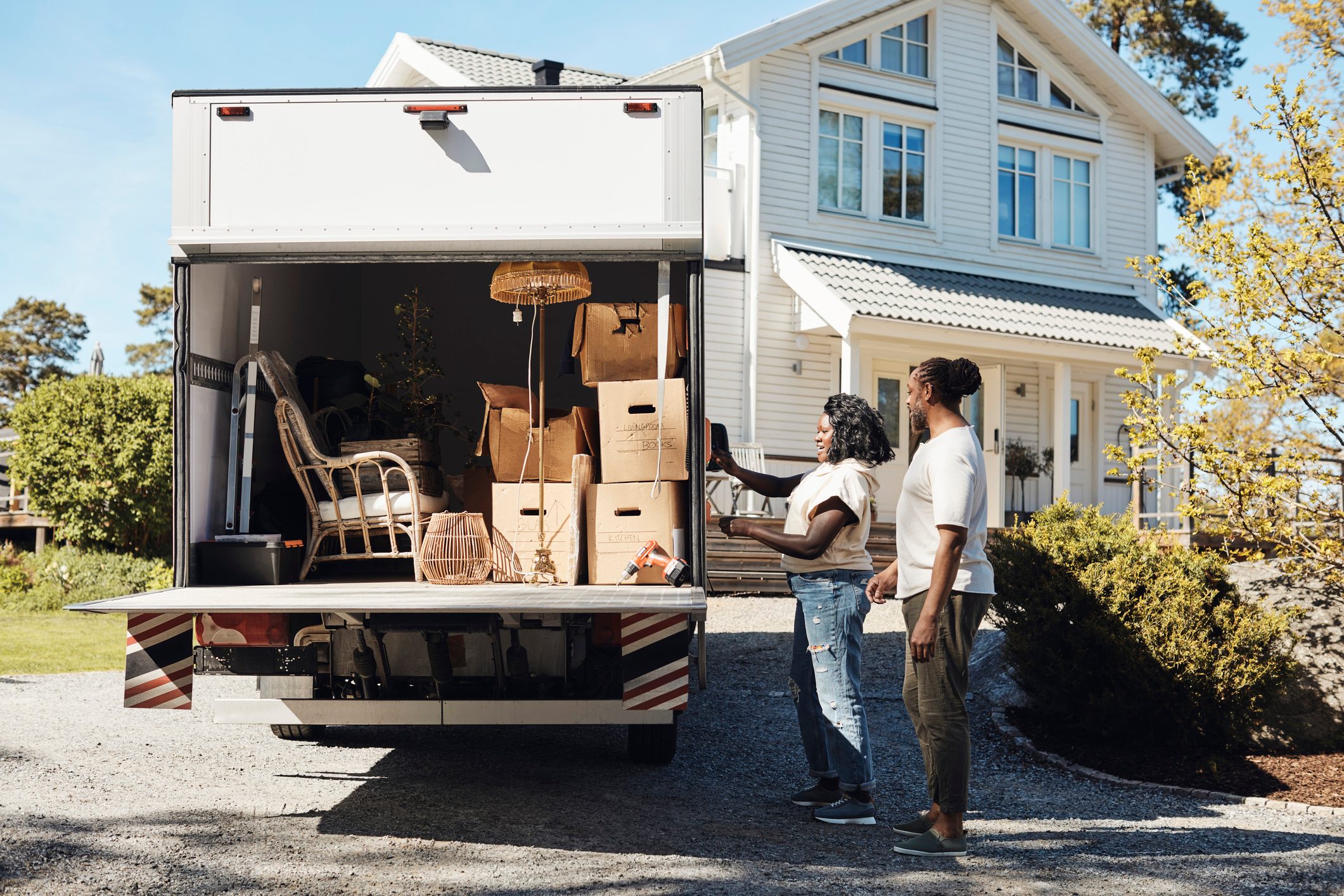 Side view of couple opening trunk of van while standing in front of house