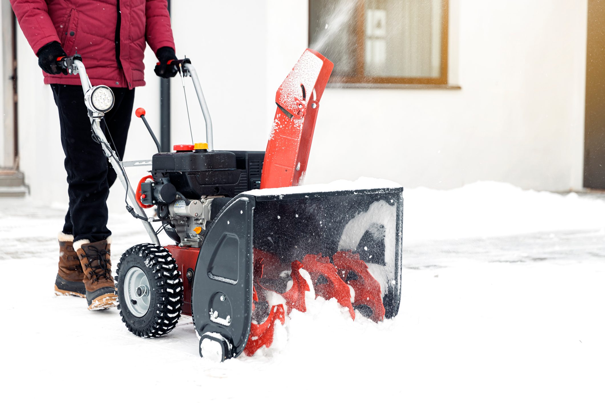 Man using red snowblower machine outdoor. Removing snow near house from yard