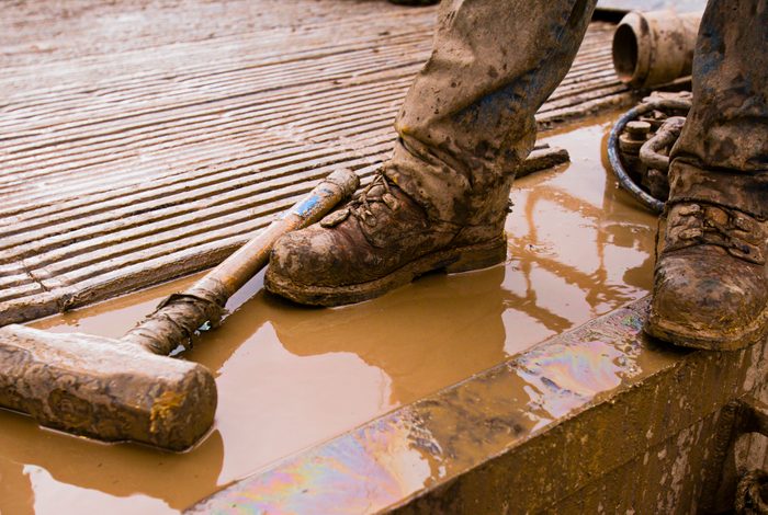 Workman standing on oil drilling platform, low section