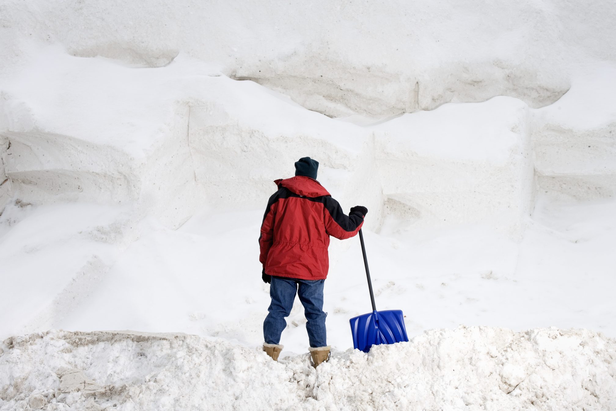 Man with snow shovel facing large pile of snow, rear view