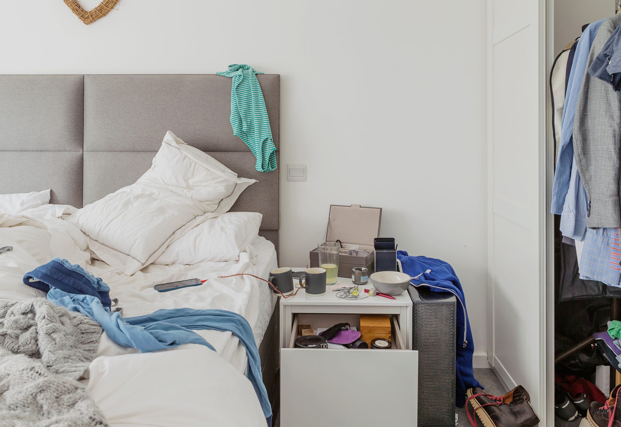 apartment bedroom with clutter on night table, bed, and floor