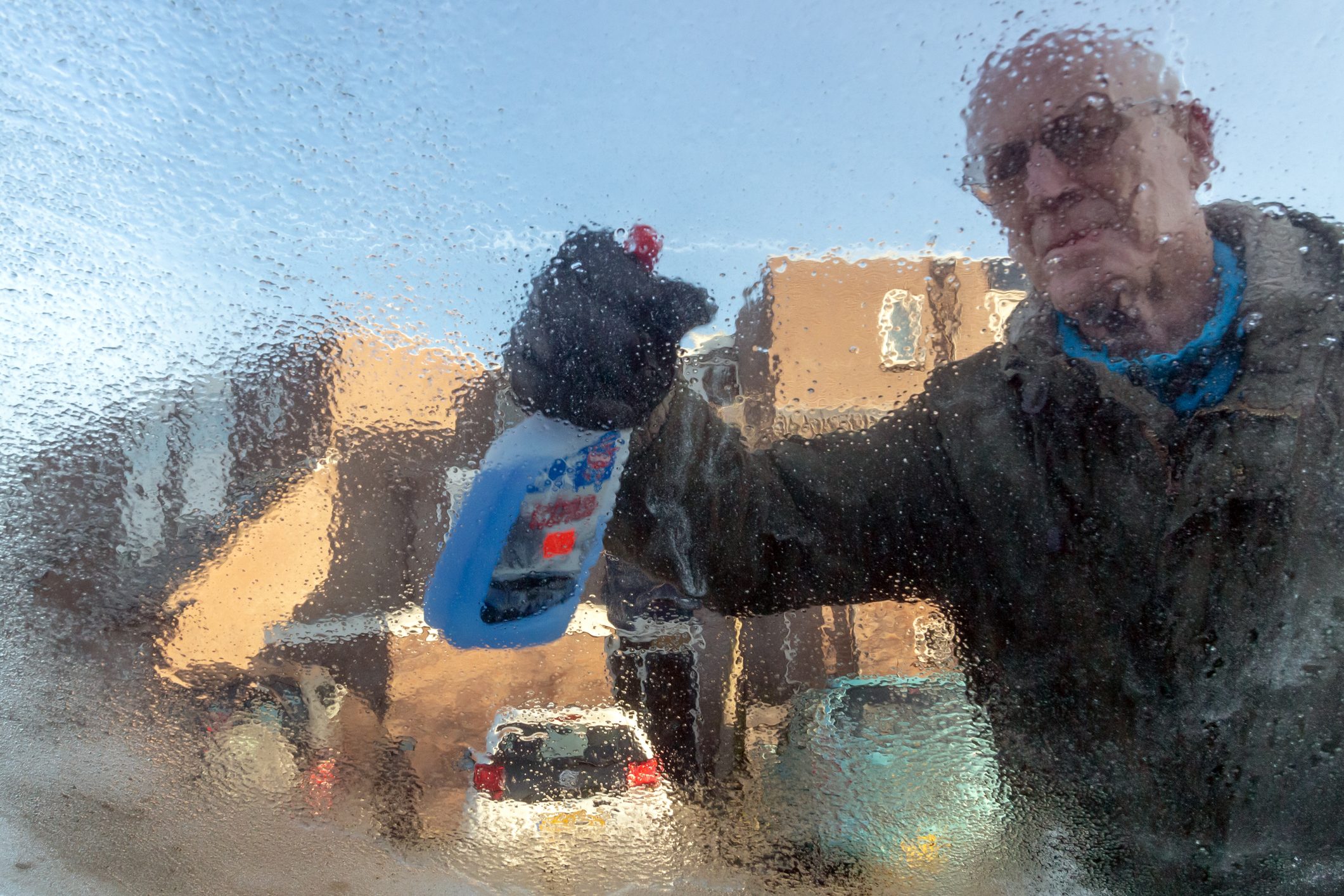 Senior de icing his car window with a bottle of antifreeze spray .