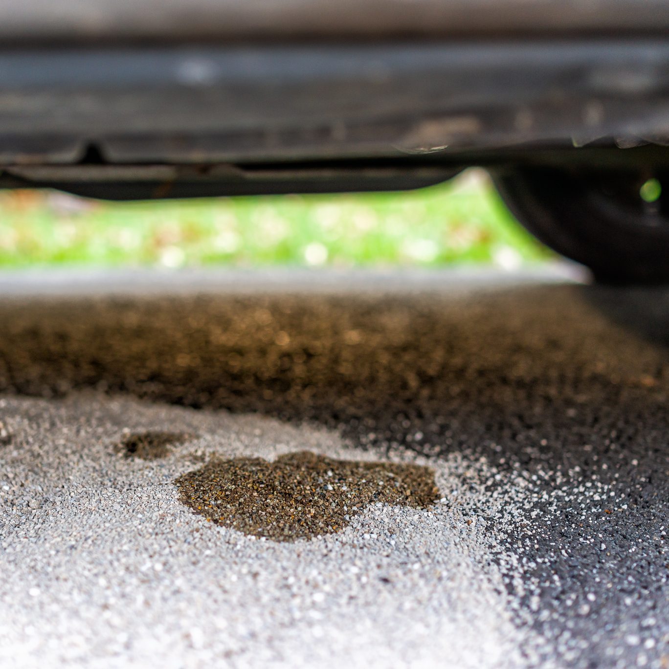 Parked car in driveway with macro closeup of vehicle leaking fuel on cat litter to prevent damaging pavement and to absorb the gas