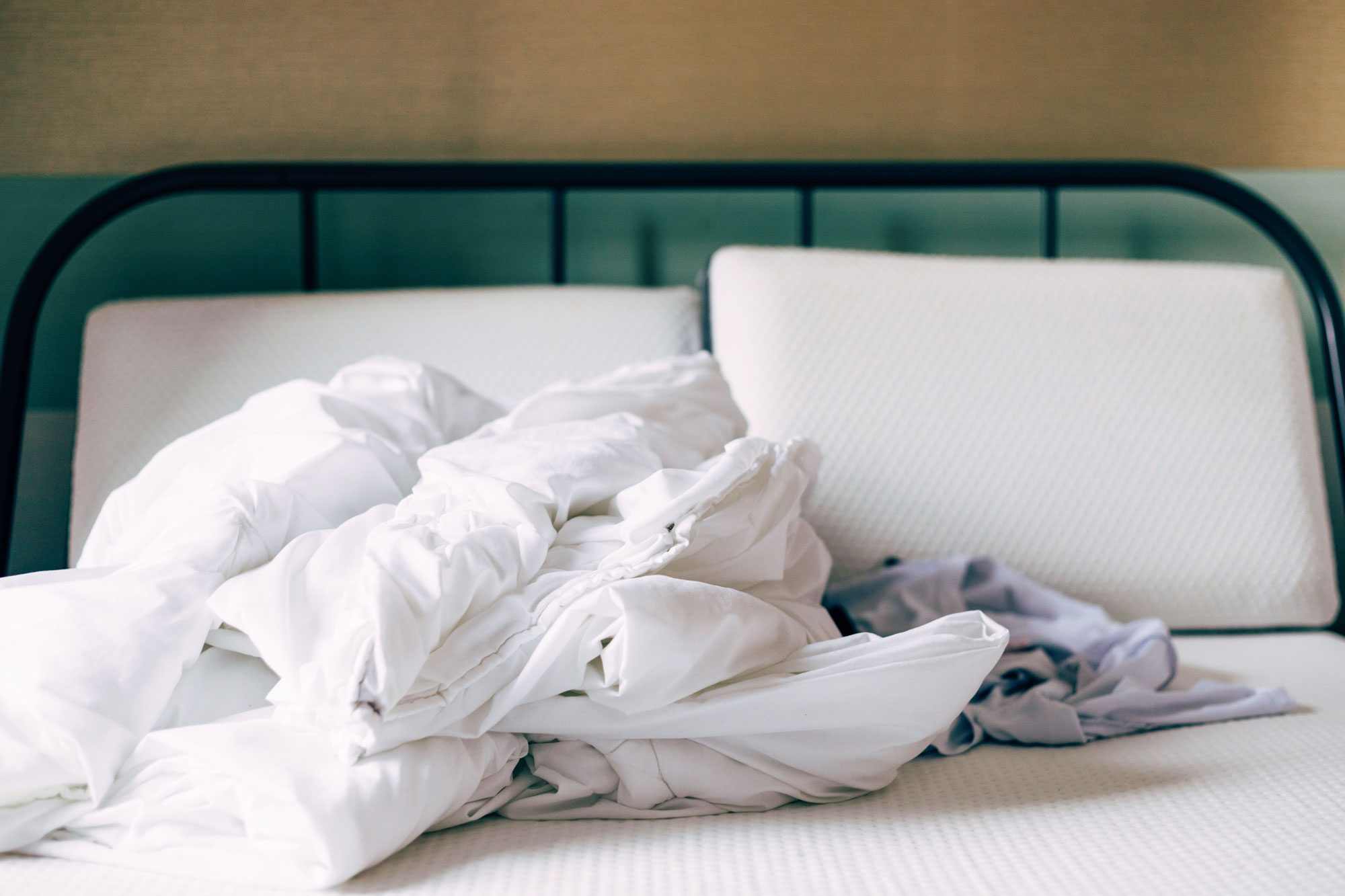 bed with sheets and pillow cases stripped in a pile on the bed