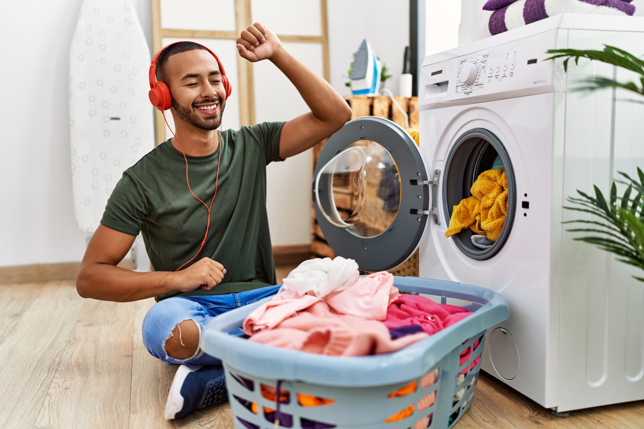 Young hispanic man listening to music using washing machine at laundry