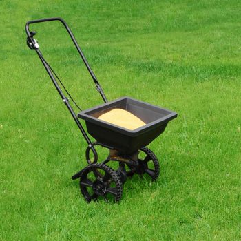 lawn fertilizer spreader filled with sulfur in a backyard with beautiful grass