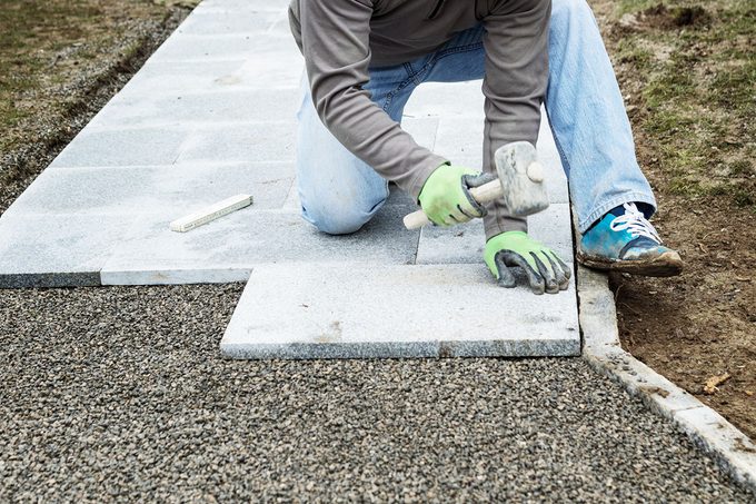 Worker Hammering The Stone Plates To Install Footpath At Garden