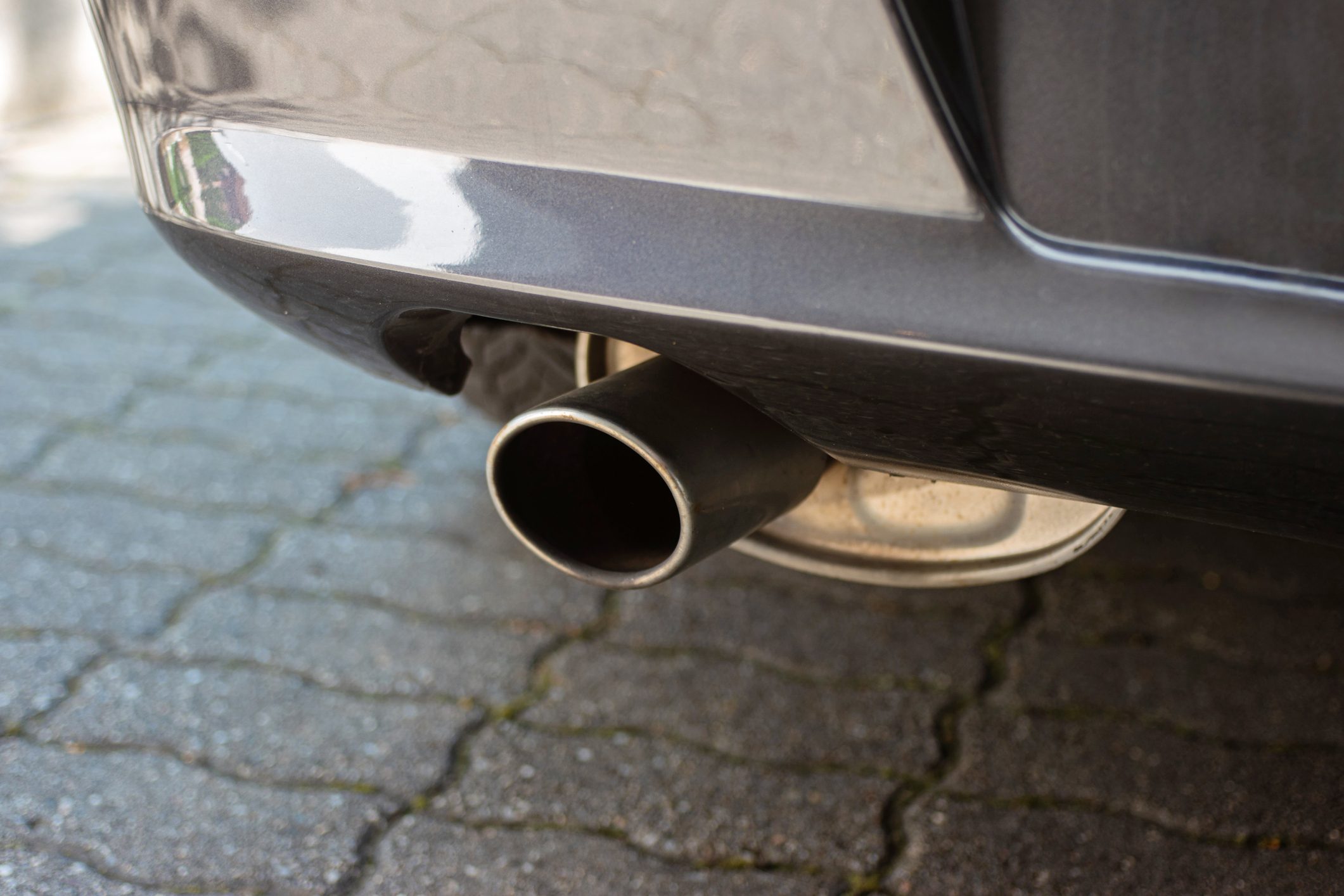 Car engine single exhaust metal tip close up shot next to rear bumper