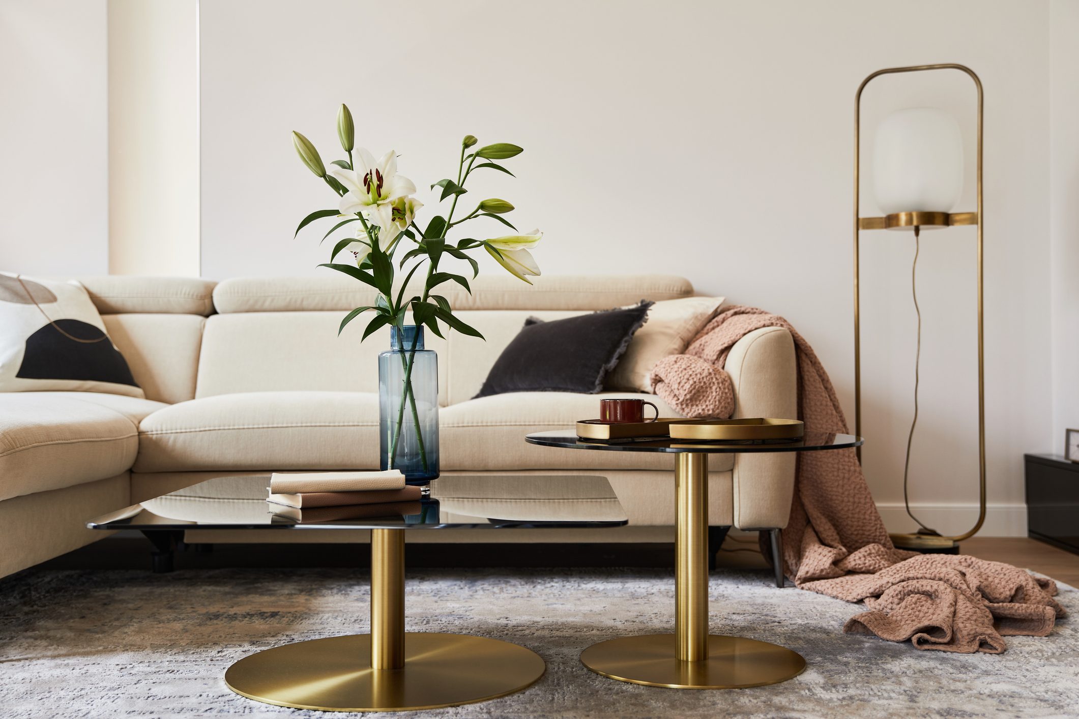 Stylish living room interior composition with beige sofa, glass coffee table, carpet on the floor and glamorous accessories. Template.