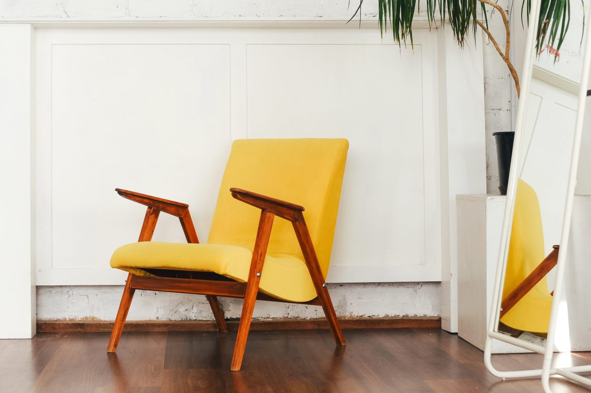 Yellow armchair and indoor flower against a white brick wall. Landscaping. Room decor. Light interior. Simplicity. Brick wall. Green palm. Home decor. Mirror.