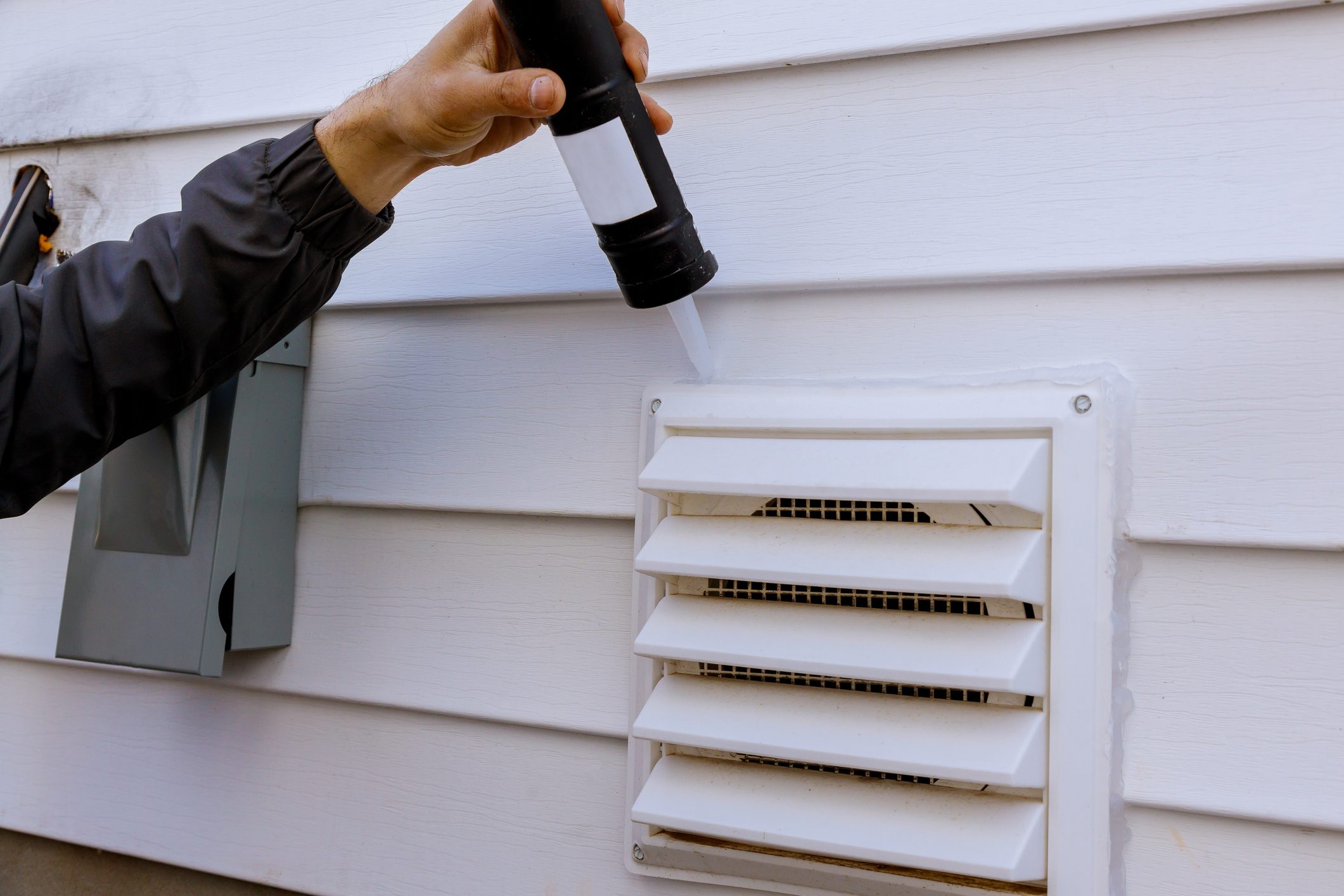 Dryer exhaust fan on side of house with plastic white trim with silicone