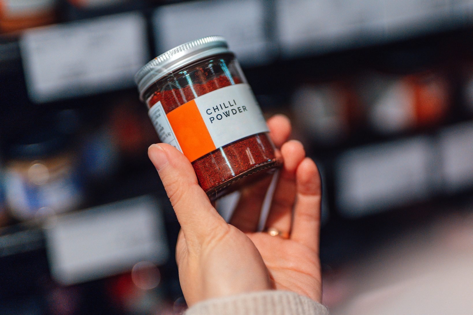 Close-up of young woman doing grocery shopping in supermarket, holding a jar of chilli powder