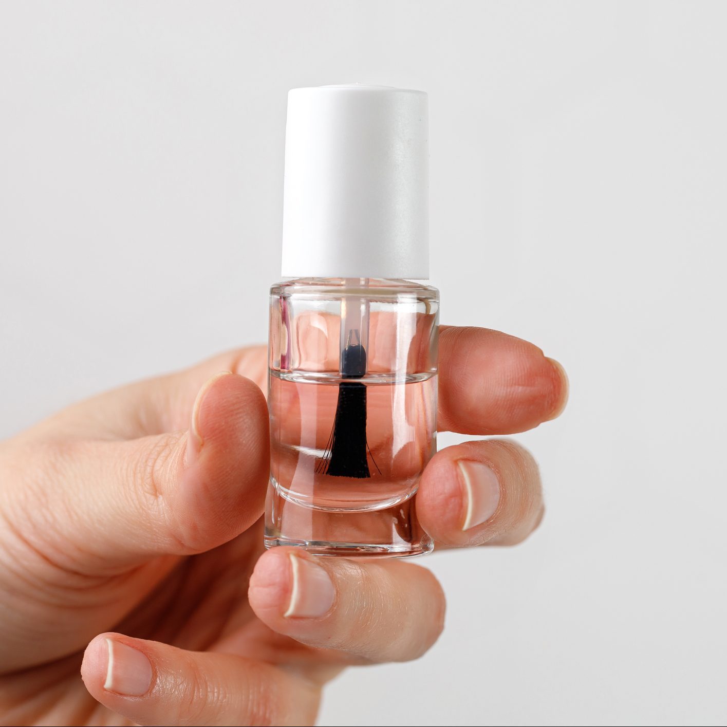 Woman's hand holding bottle of nail polish. Firming transparent nail polish in female hand.