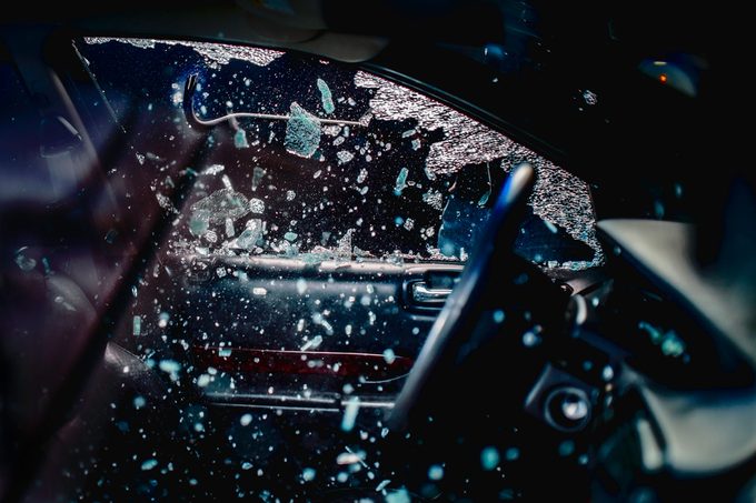Car thief using a work tool to break into car, many jagged glass pieces flying through the air