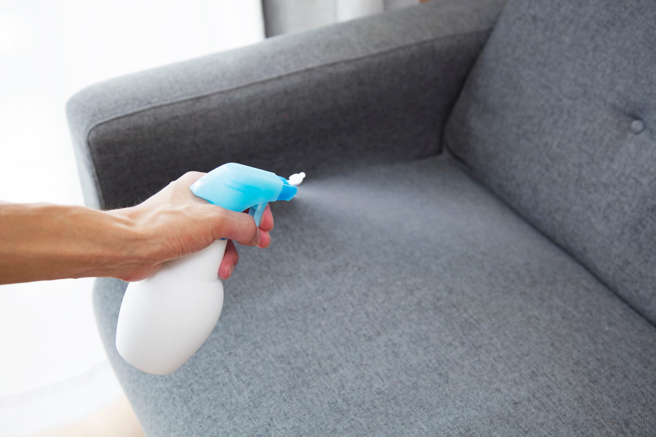 Sprayed air freshener in hand on home interior background