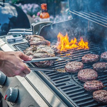 Marinated Lamb Joint And Beef Burgers Cooking On A Barbecue gas grill