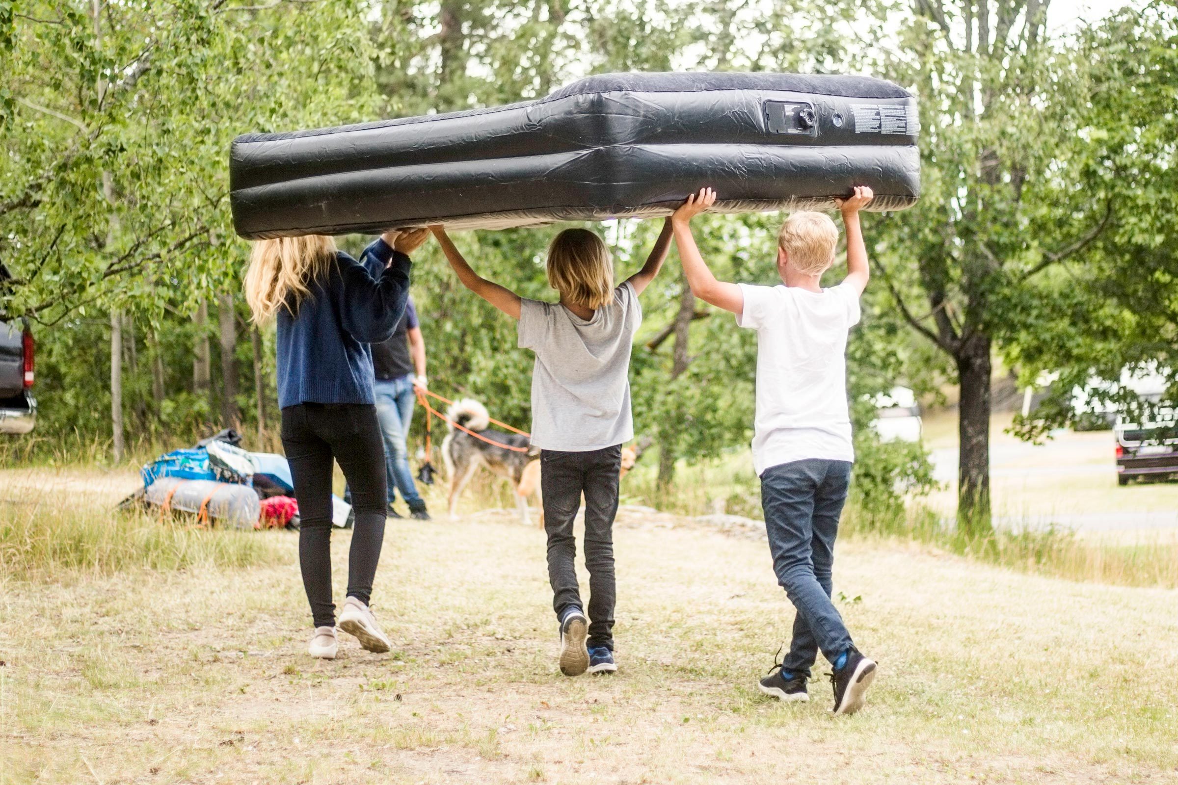 Children Carrying Inflatable Mattress While Walking Towards Car At Camping Site