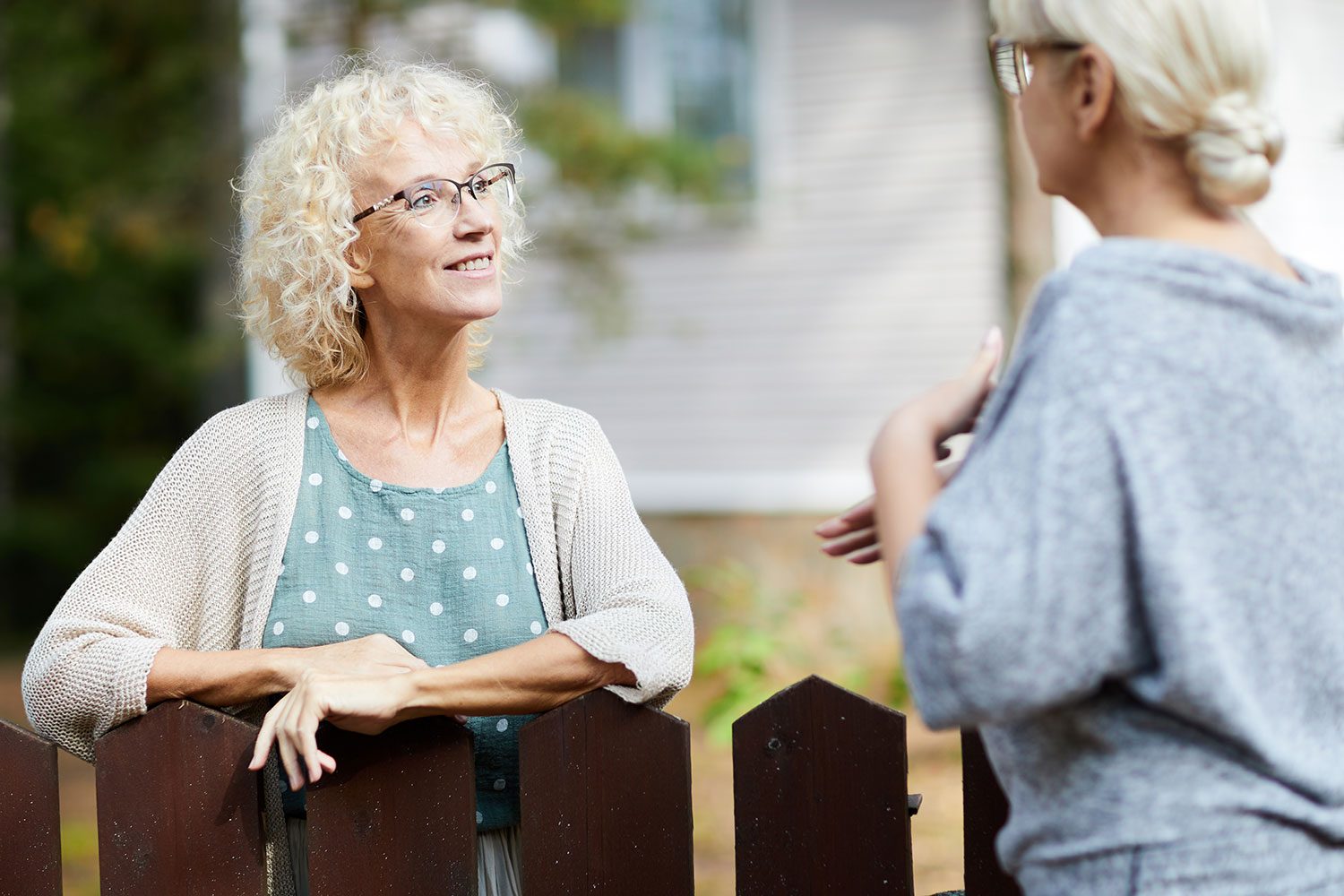 Two mature female neighbours talking through fence about everyday life stuff