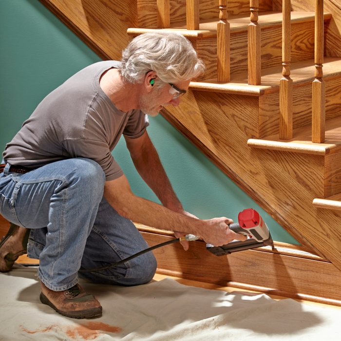 man using a nail gun on trim near a stair case