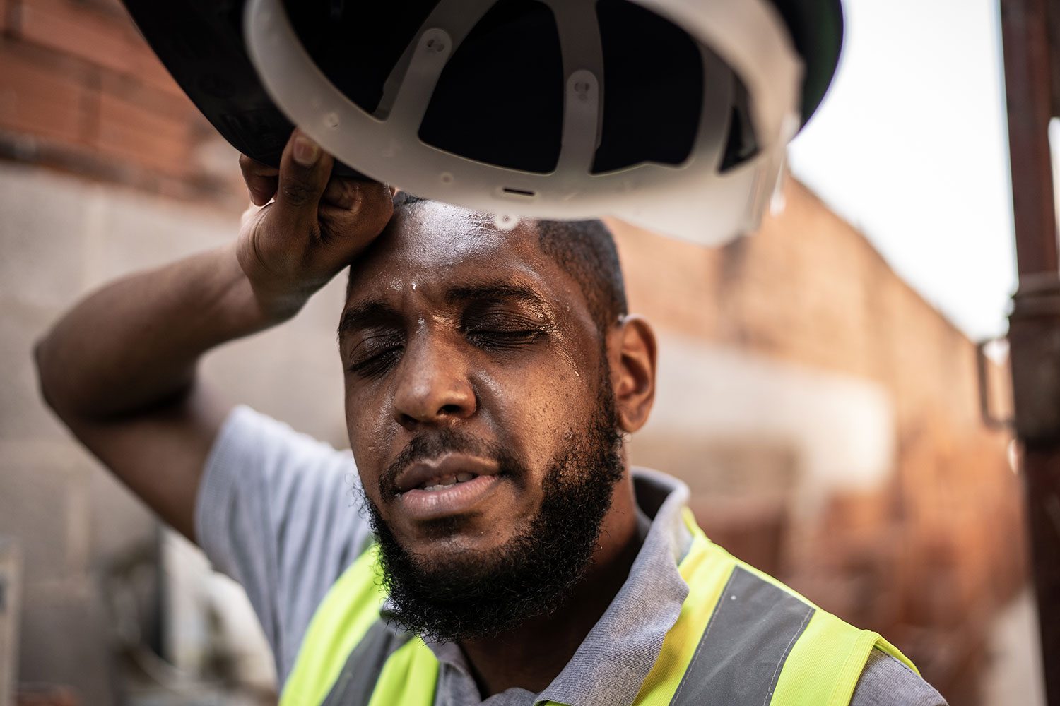Exhausted Construction Worker Sweating At Construction Site with hard hat in hand