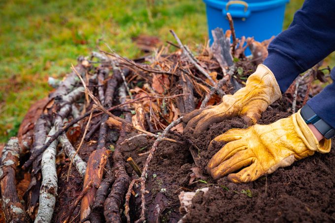 Close Up Photo Of A Person With Yellow Gloves Adding Dirt To The Top Of A Hügelkultur Mound