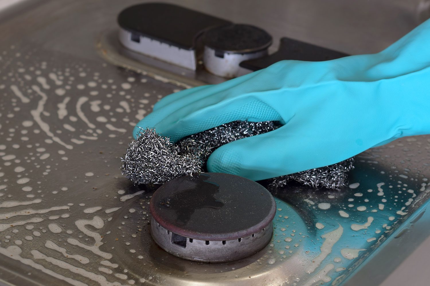 Person's Hand In Rubber Glove Cleaning Gas Stove Top with steel wool scrubber