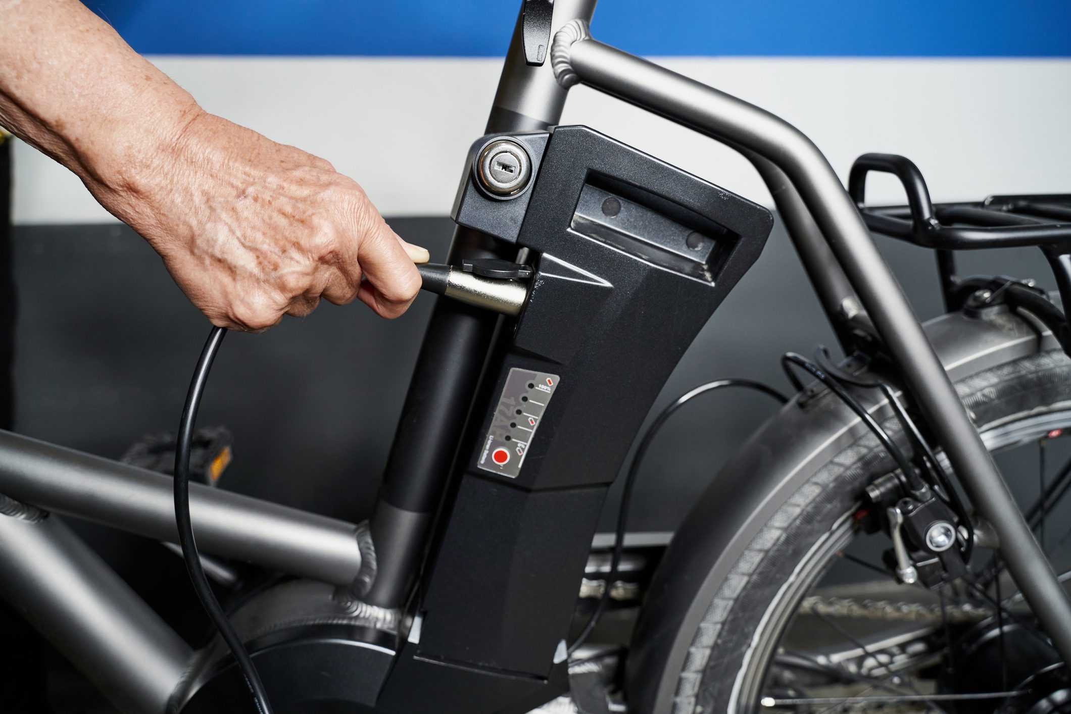 Hand of caucasian man charging battery pack on electric bicycle at garage. Transport concept.