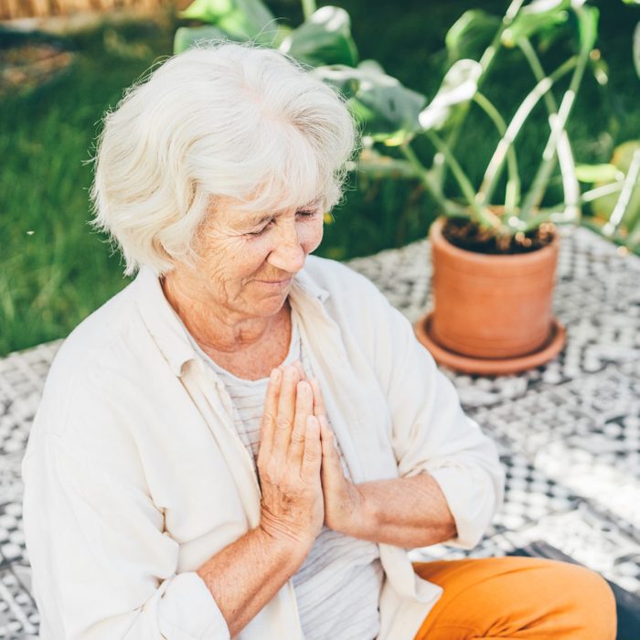 Senior woman doing yoga in the backyard at sunny day.