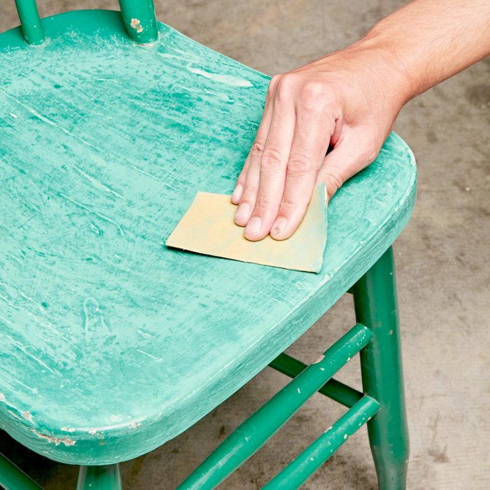 using sand paper on a green chair