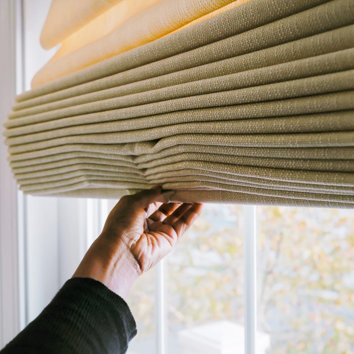 hand pulling down Thermal Curtains to cover window and save energy