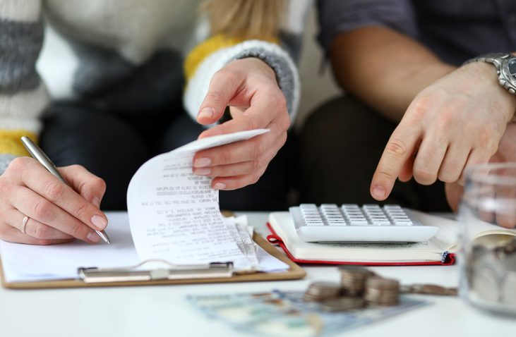 Close-up view of man and woman making account of family income by Writing down and calculating expenses