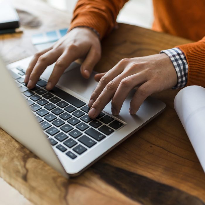 Close-up of man using laptop next to construction plan at desk