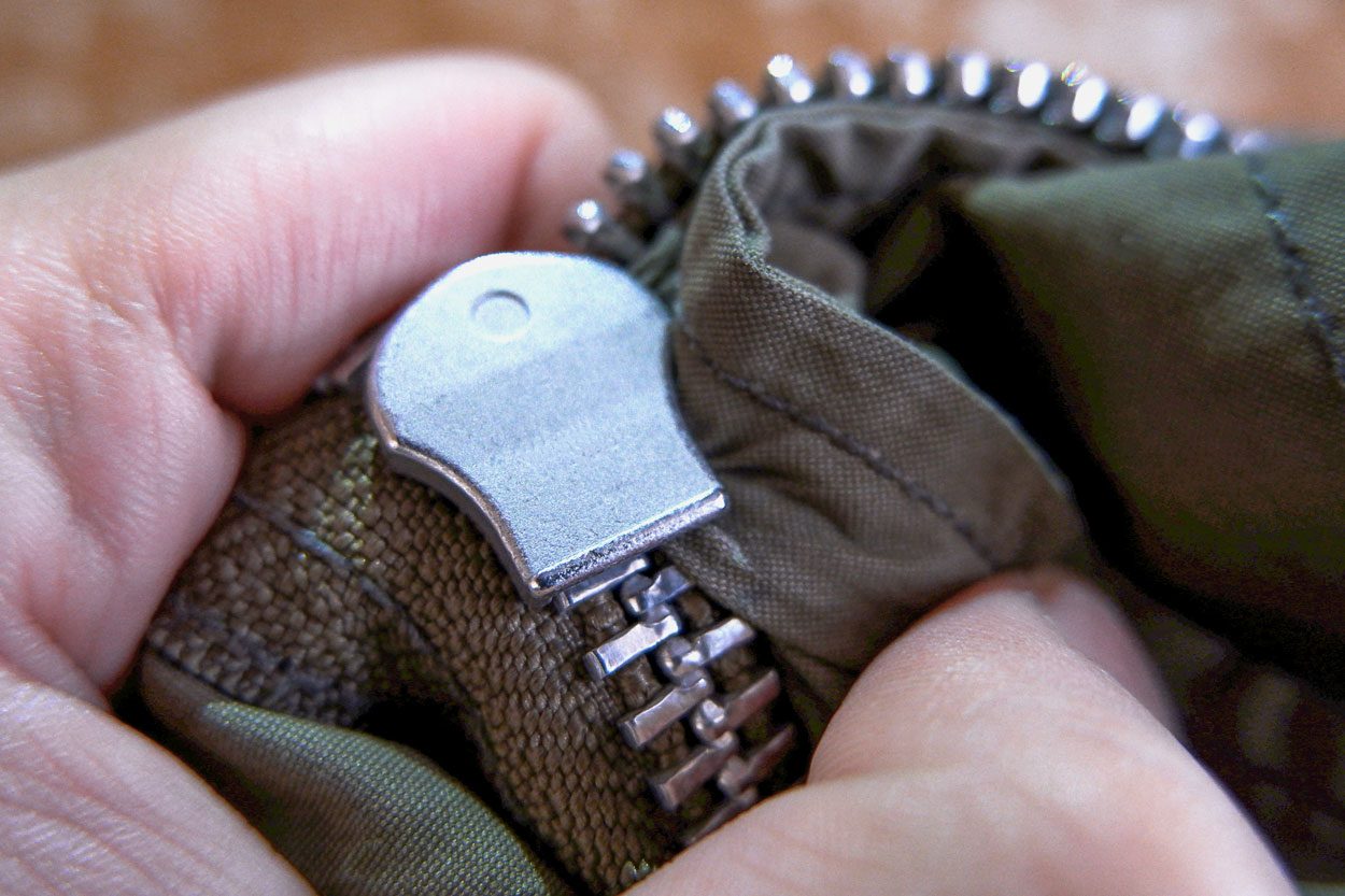 A close up of stuck zipper on a dark green jacket, holding by a hand