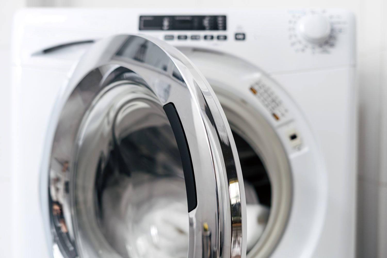 open door in automatic washing machine and clean clothes inside after laundry in apartment
