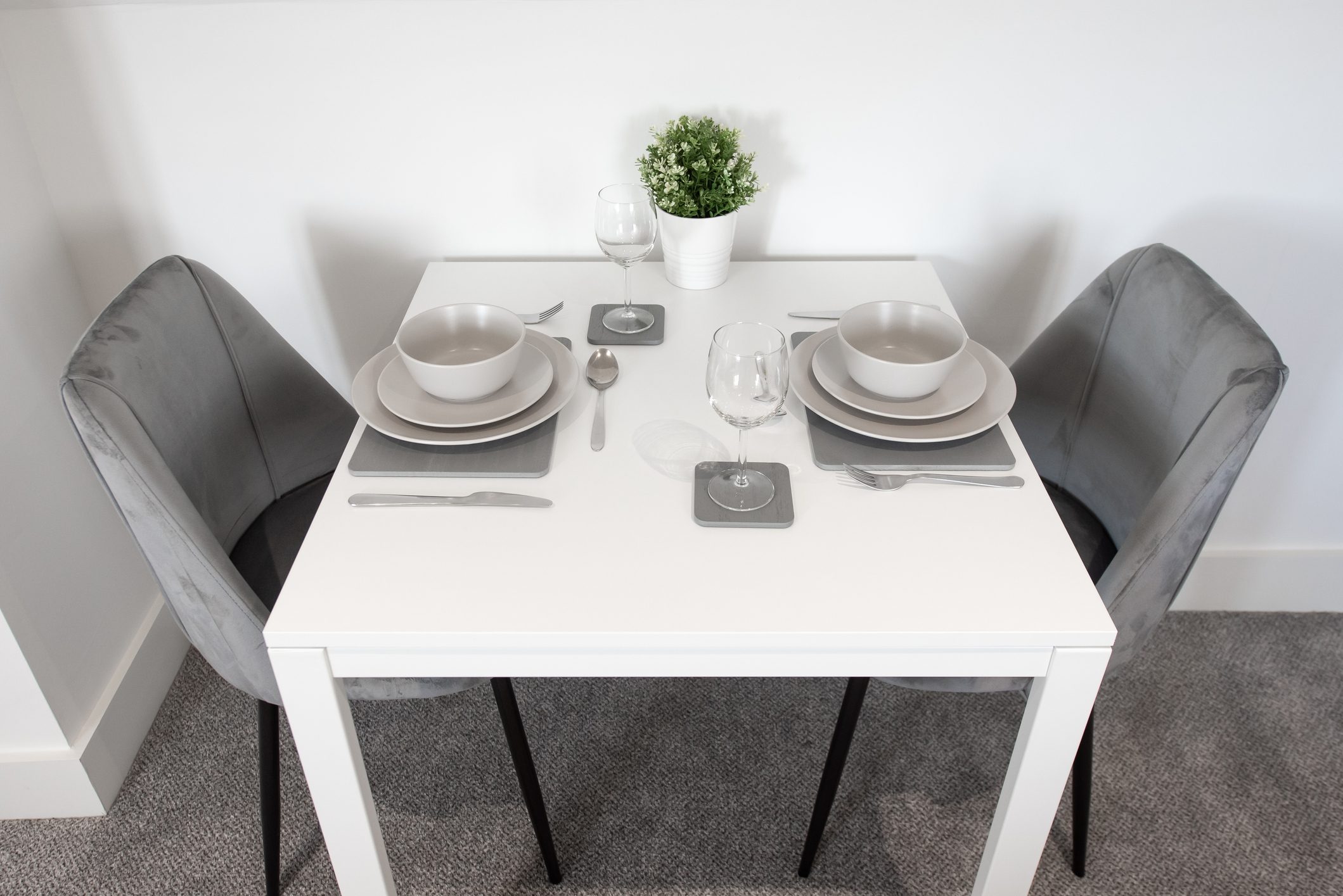 A general view of a dining table with a place setting, plain grey dinner set, plate, bowl, place mat, wine glass and cutlery