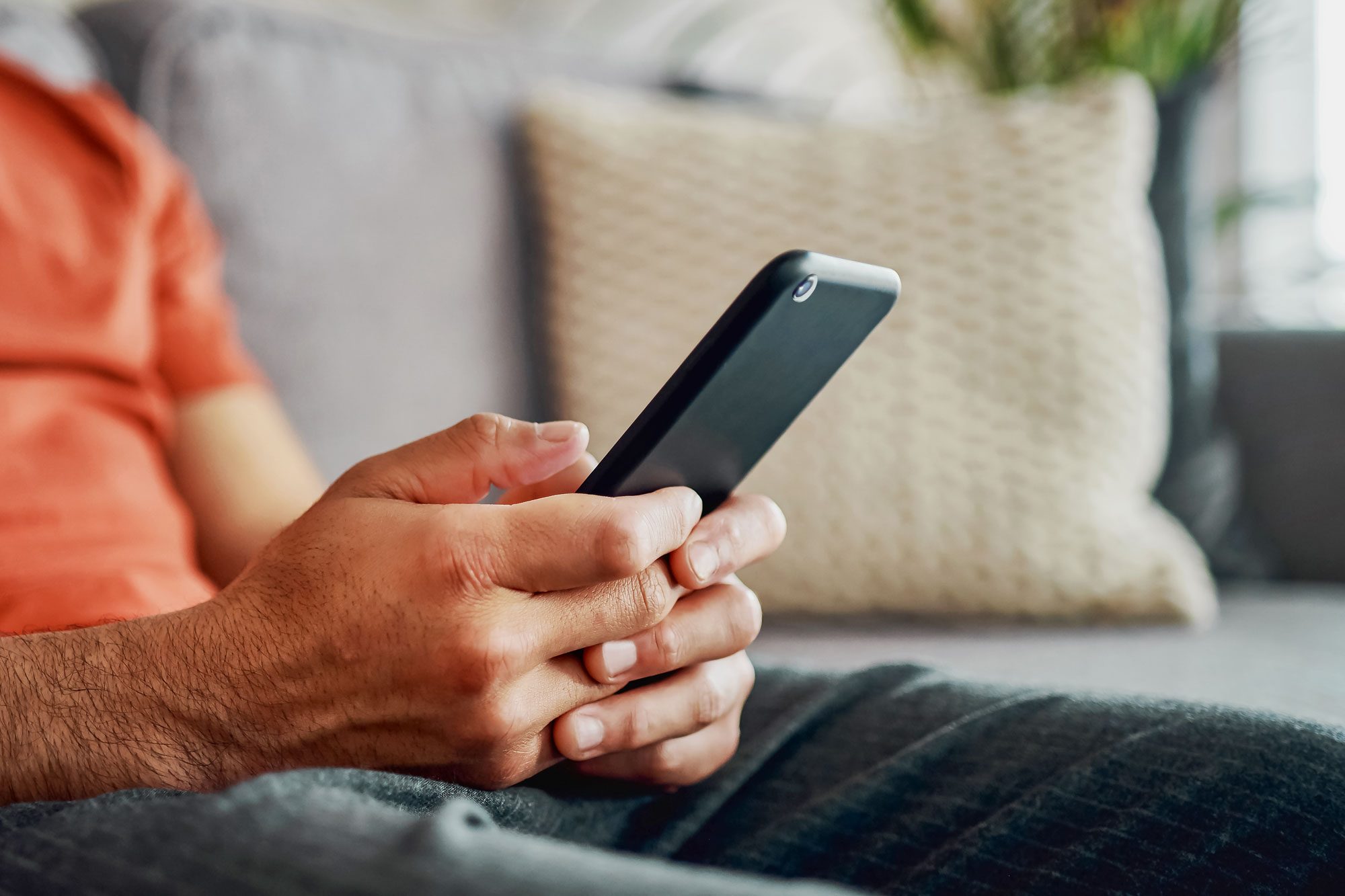 Cropped Shot Of An Unrecognisable Man Sitting Alone In His Living Room At Home And Using His Cellphone