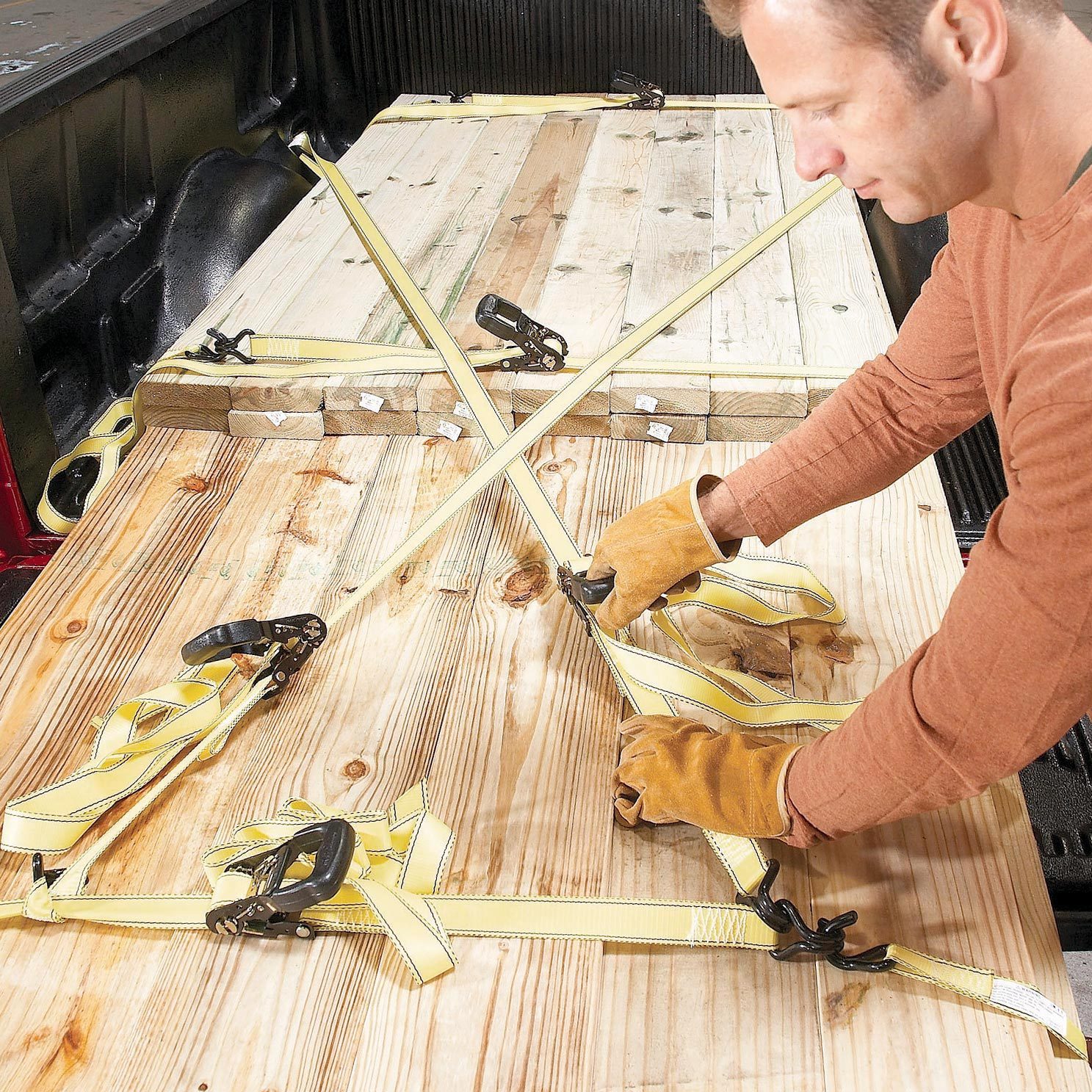 man strapping down lumber in pick up truck with yellow straps