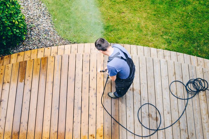 Professional Pressure Washing Cleaning Service Man Sprays Terrace Deck or Patio With High Pressure Water with a Power Washer to Remove Dirt and Debris From the Wooden Surface