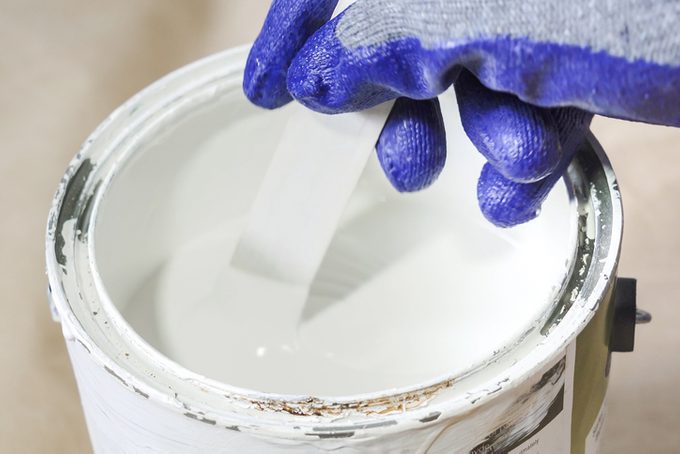 Close up of hand gloved painter mixing paint in metal paint can with wooden paint stick
