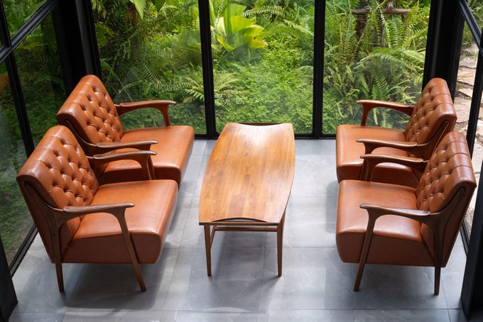 room with a brown sofa and chairs sitting in front of a large window in a wooded area