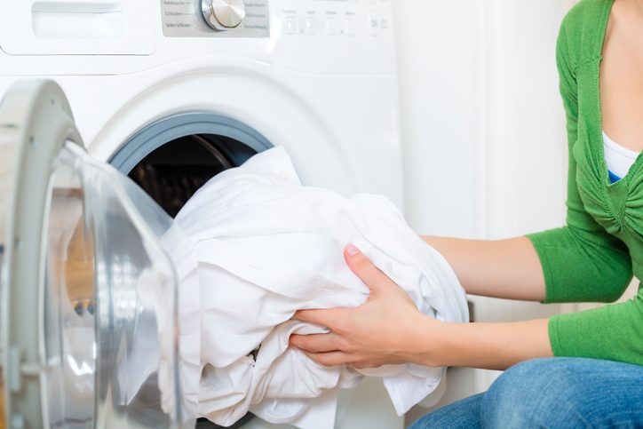Young Woman Unloads a load of white laundry out of the washing machine on laundry day in a bright laundry room
