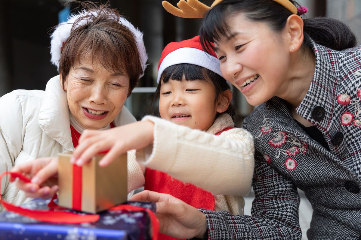 Multi Generation Family Enjoying Christmas by Wrapping Presents together and wearing fun, festive accessories