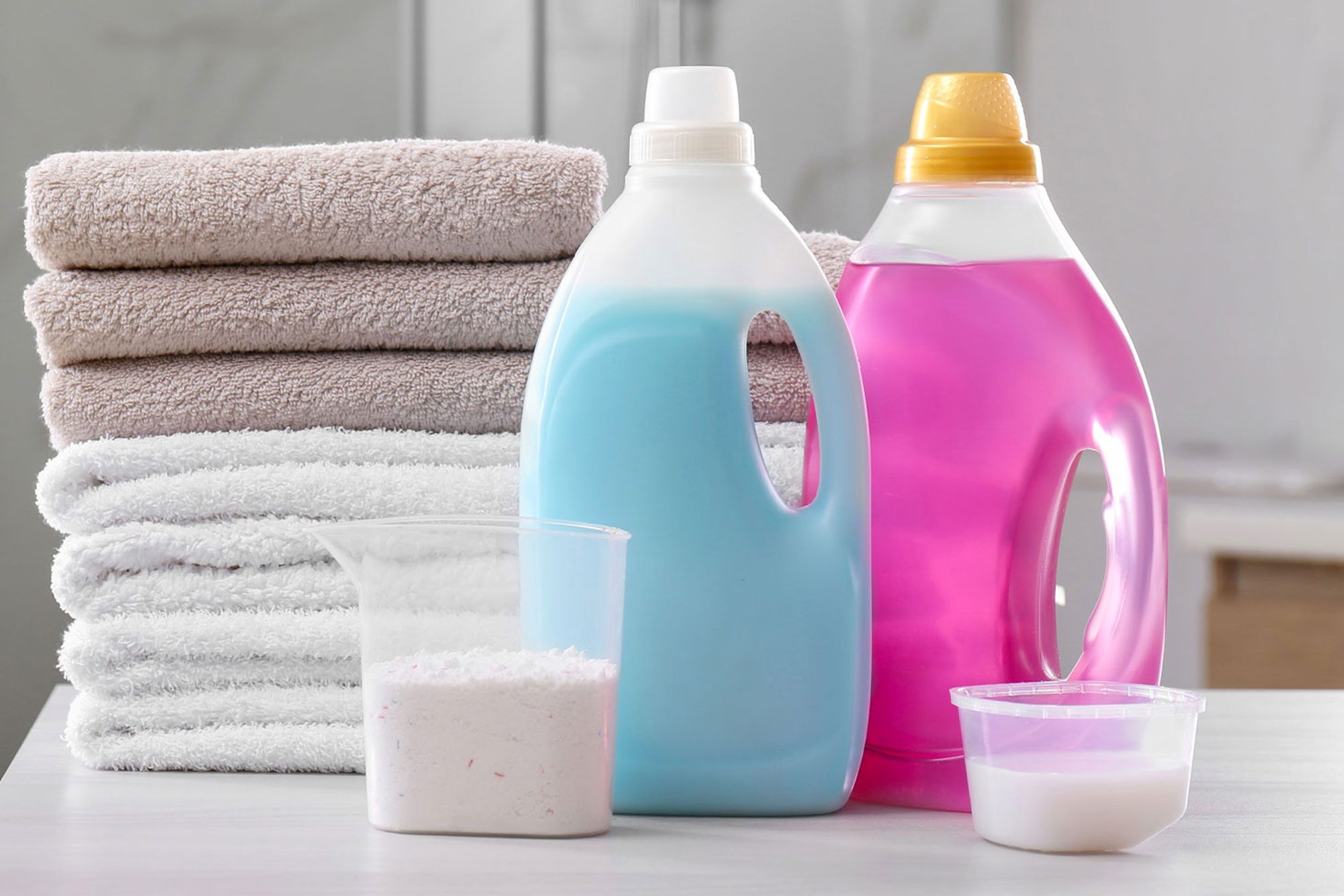 Stack Of Folded Towels And Detergents On White Table And Washing Machine In Background