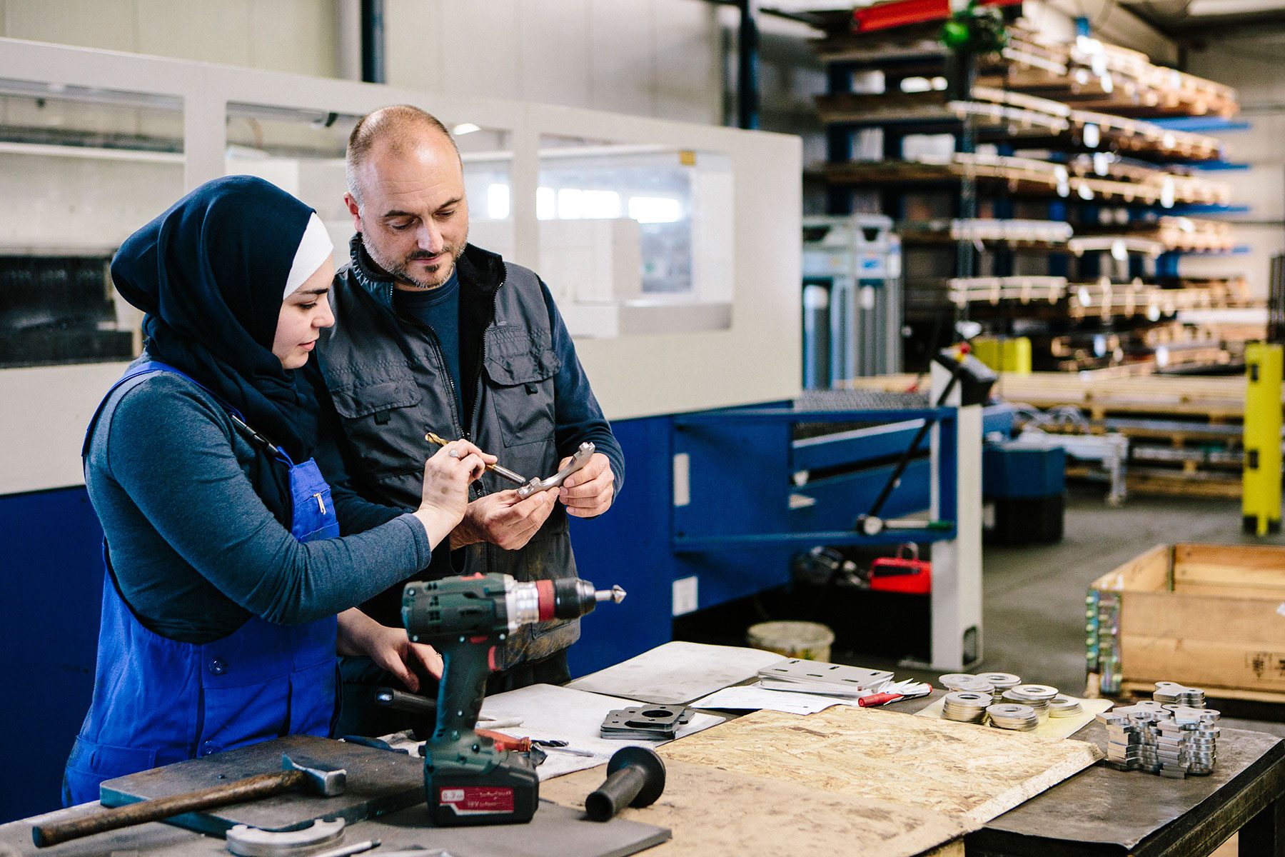 Teamwork: technician explains a work tool to a young woman in a workshop