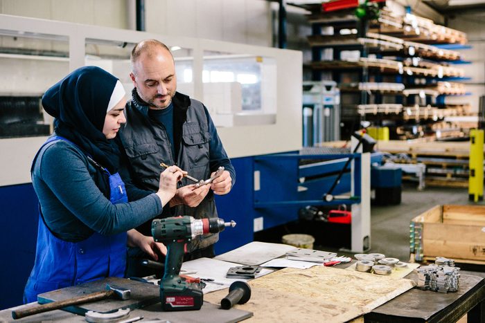 Teamwork: technician explains a work tool to a young woman in a workshop